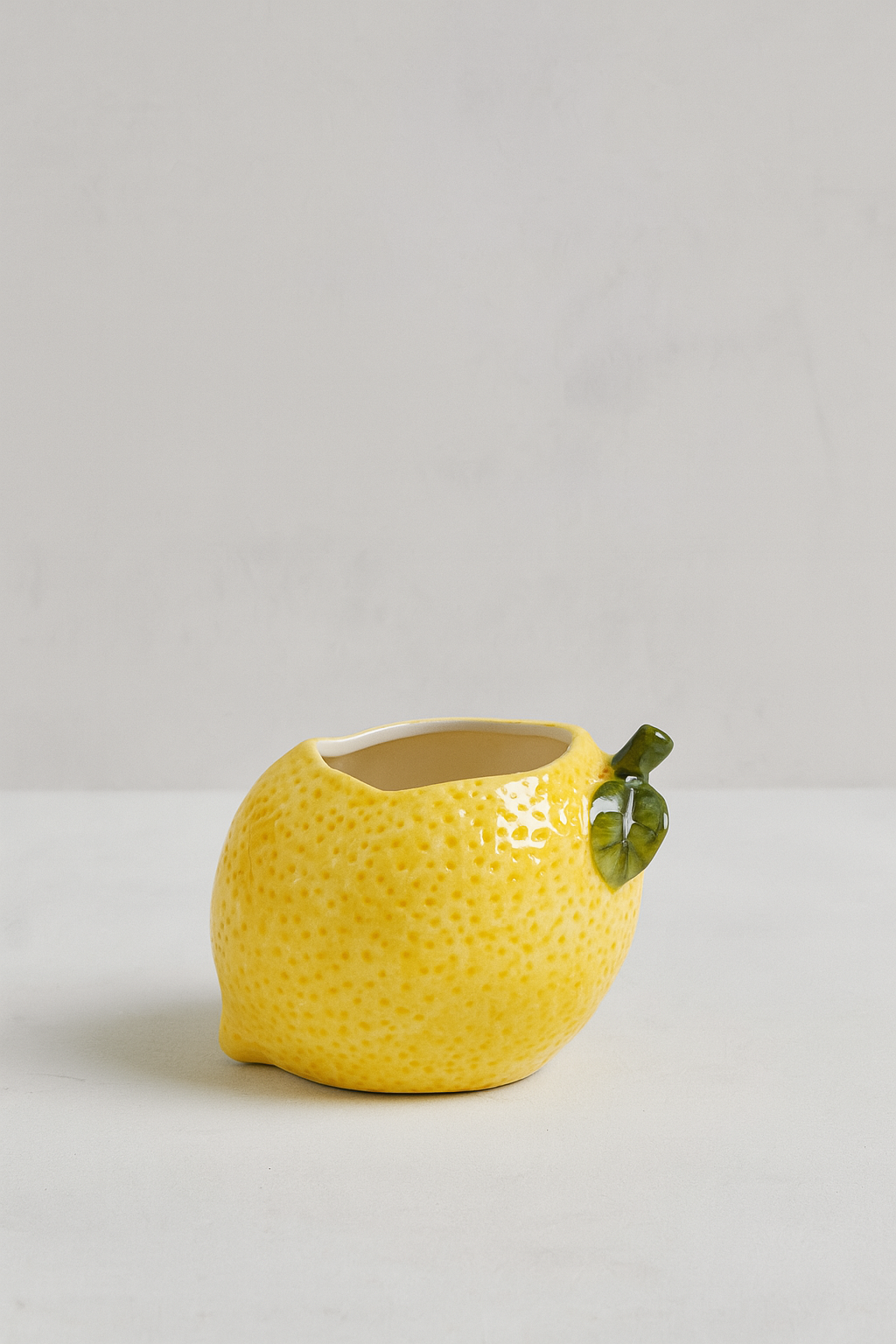 Yellow ceramic lemon-shaped planter with a green leaf on a light gray background