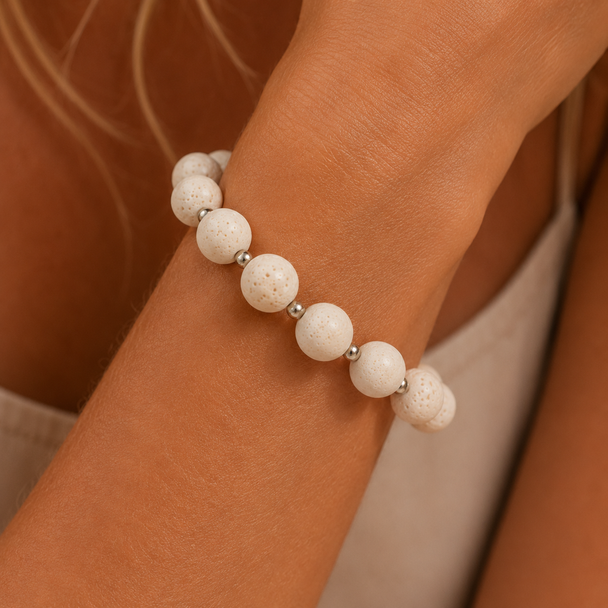 A close-up of a person's wrist wearing a beaded bracelet made of matte white stone beads separated by small silver spacer beads.